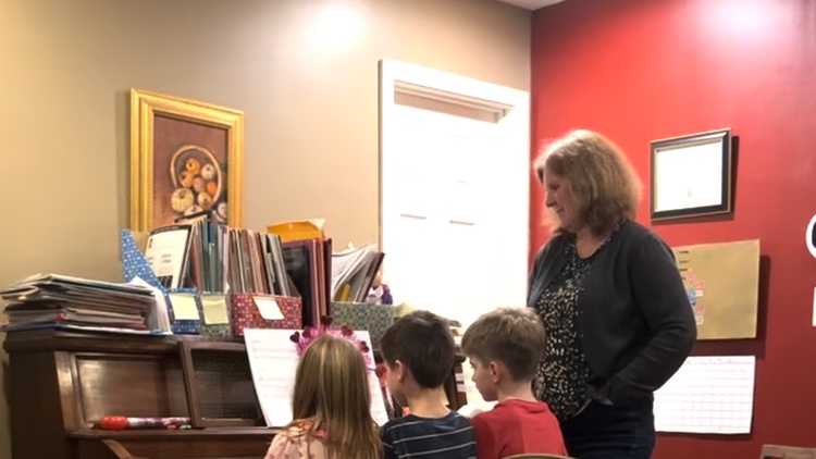 Piano teacher standing next to two students playing the piano